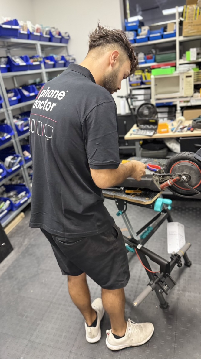 Phone-Doctor-Mitarbeiter arbeitet an einem geöffneten E-Scooter auf der Werkbank